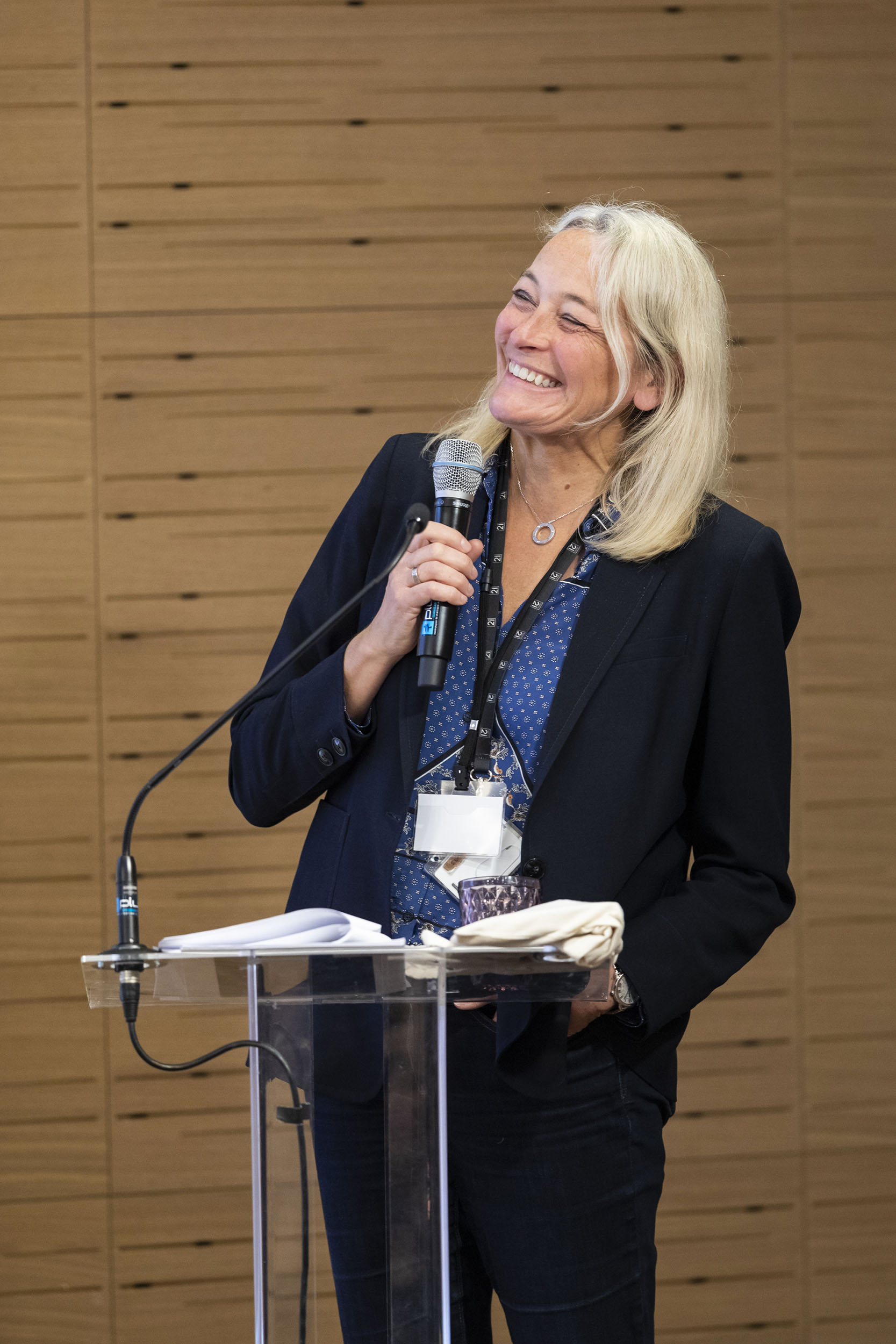Portrait de la Mme. Stéphanie Lagalle-Baranès, DG de l'OPCO2i pendant son intervention au pupitre lors d'un séminaire de l'entreprise, elle aborde un large sourire
