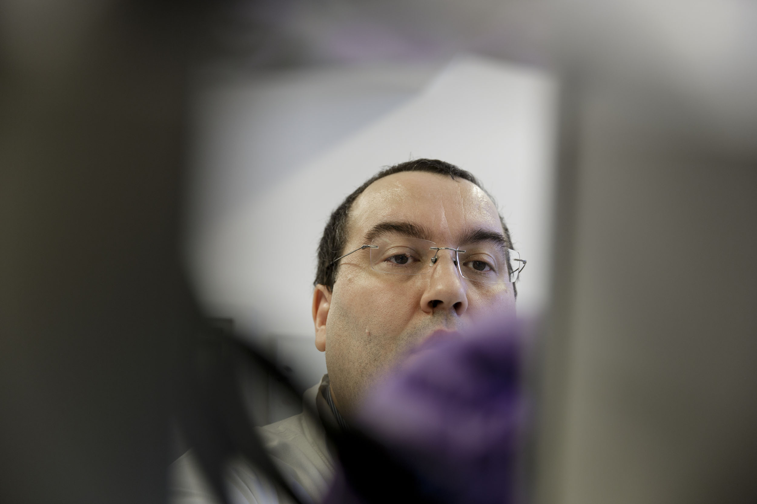 Portrait en légère contre-plongée d'un chercheur portant des lunettes dans un laboratoire de recherche, il est au centre de la photo et l'avant plan est flou