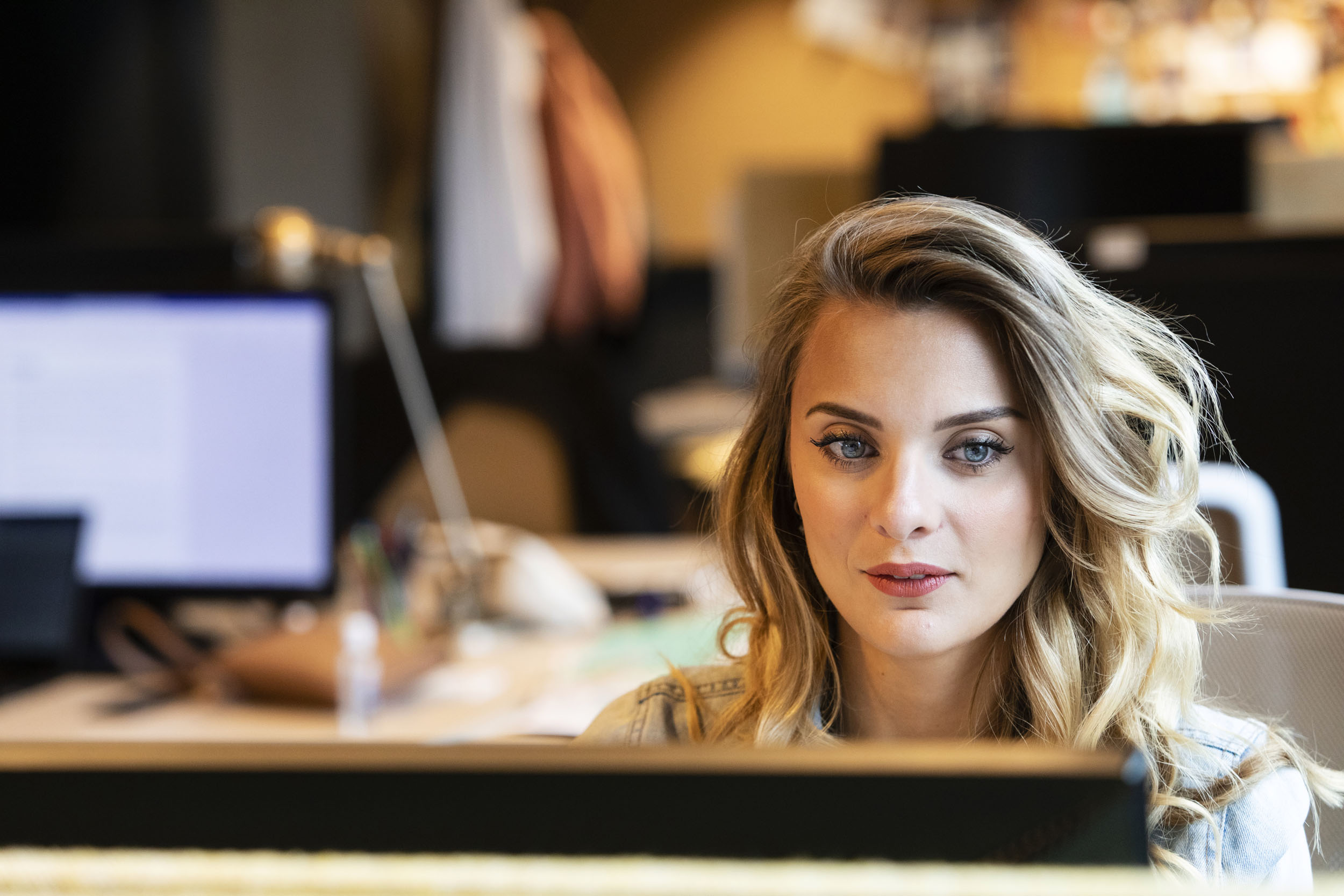 Portrait d'une femme blonde aux yeux bleus assise à son bureau dans l'entreprise, elle regarde son écran d'ordinateur