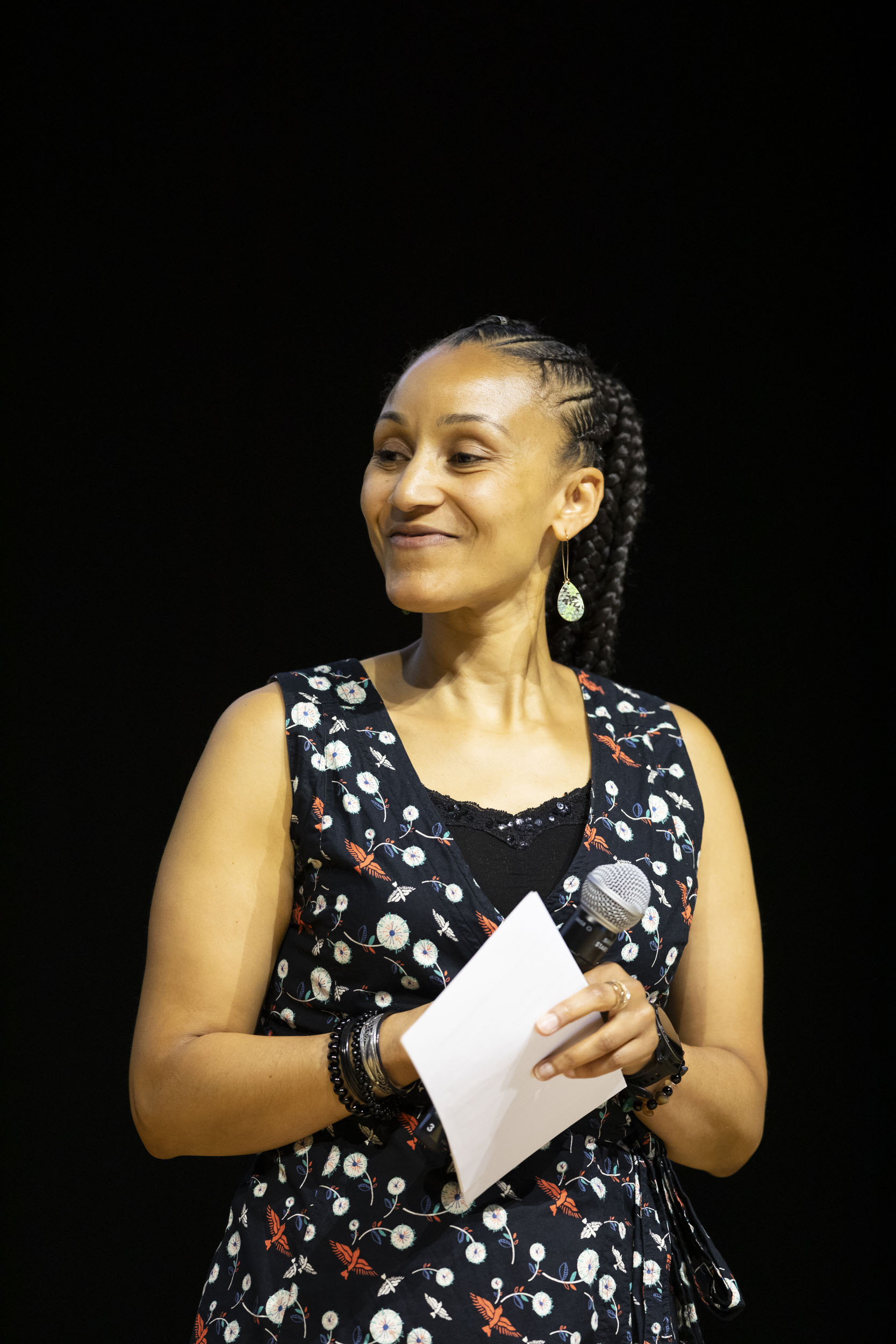 Portrait d'une intervenante en robe sur scène qui regarde le public avec son micro et ses notes à la main lors d'une convention d'entreprise