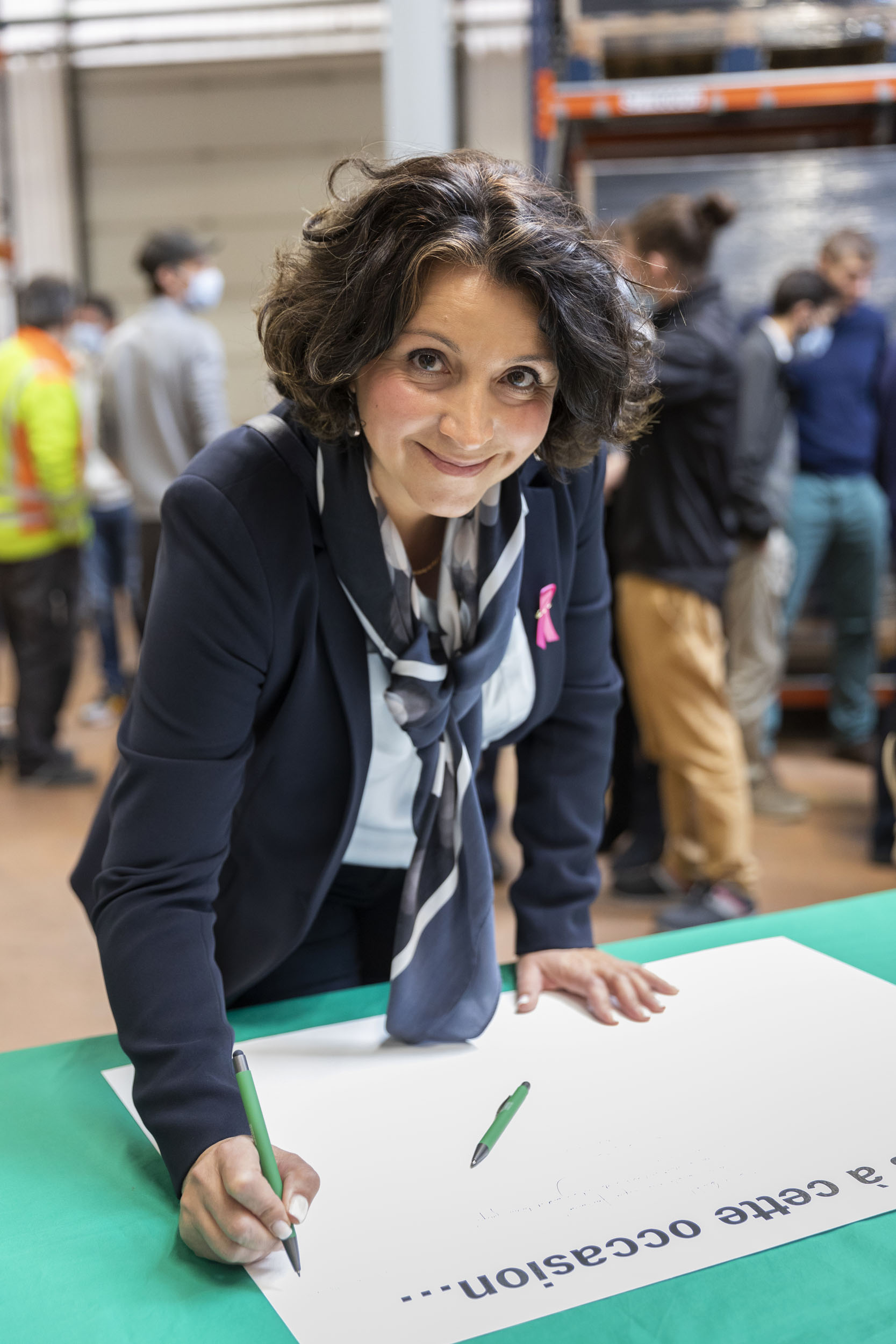Photo événementielle de portrait d'une invitée qui signe un livre d'or en regardant l'objectif lors de l'inauguration d'une ligne de production de filtres industriels