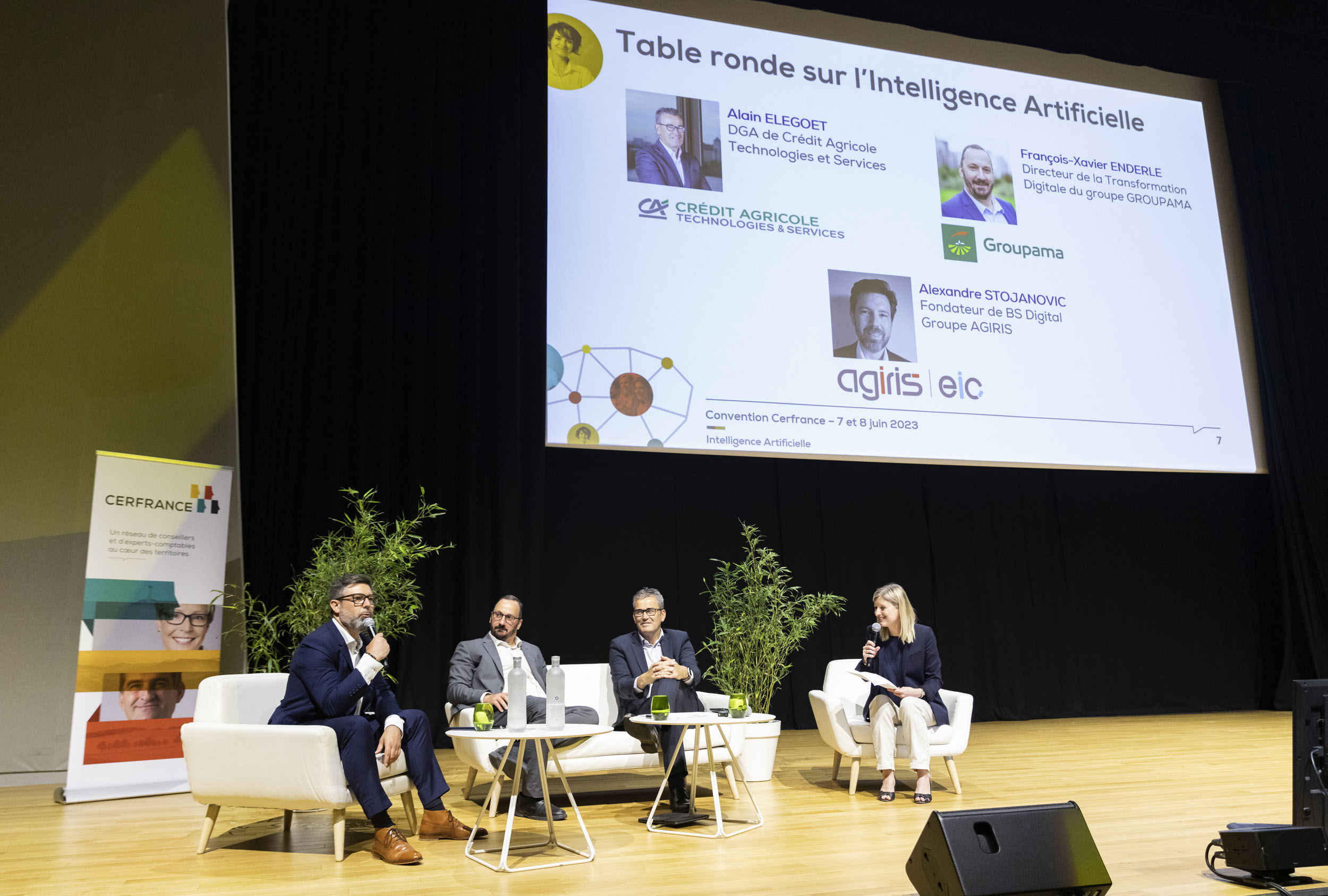 Portrait en plan large de 4 participants à une table ronde sur une grande scène pendant une convention d'entreprise