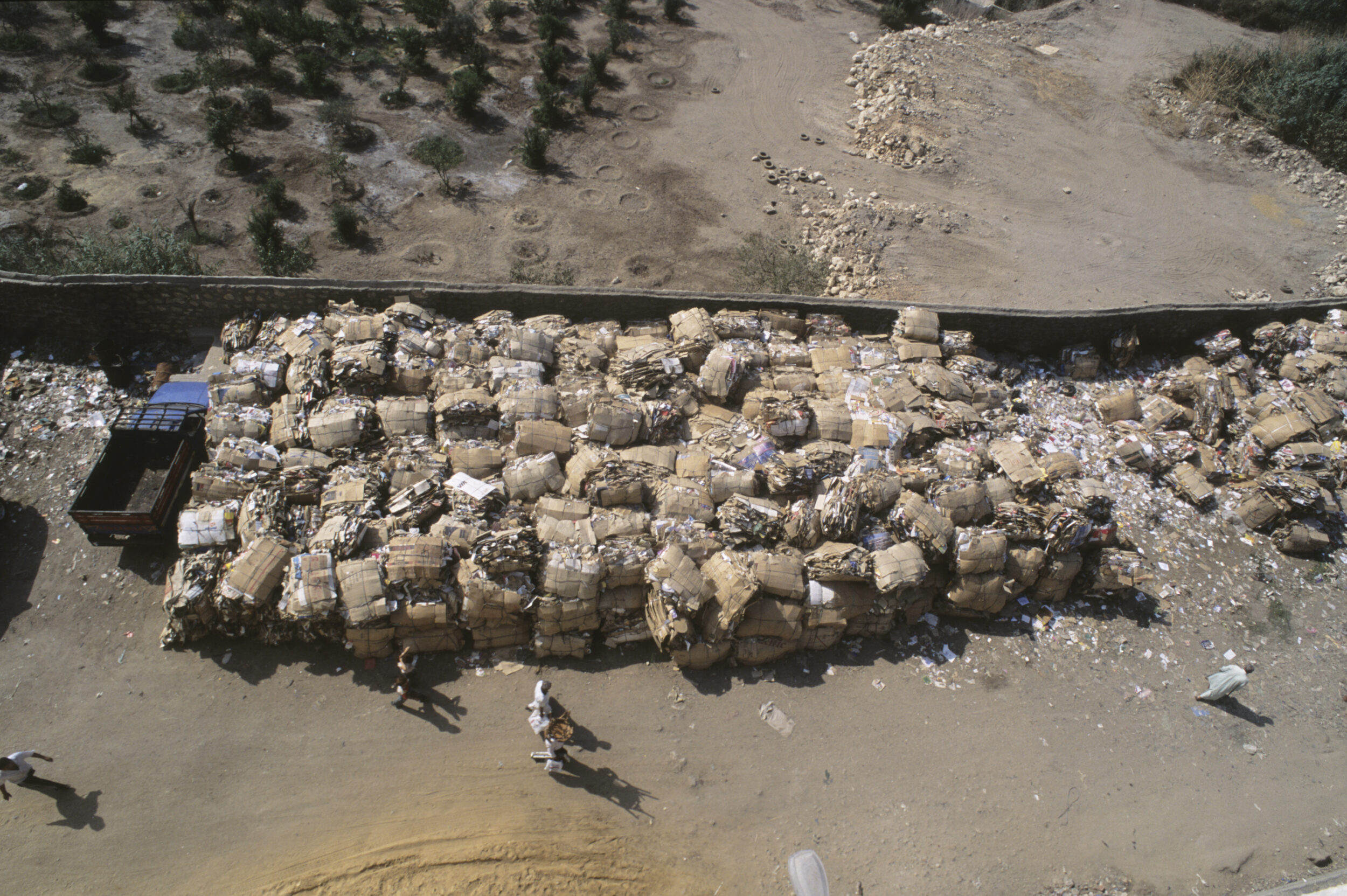 Vue en plongée d'un stock de balles de déchets triés valorisables stockés le long d'un mur dans une rue du quartier de Mokattam au Caire, des passants marchent à-côté