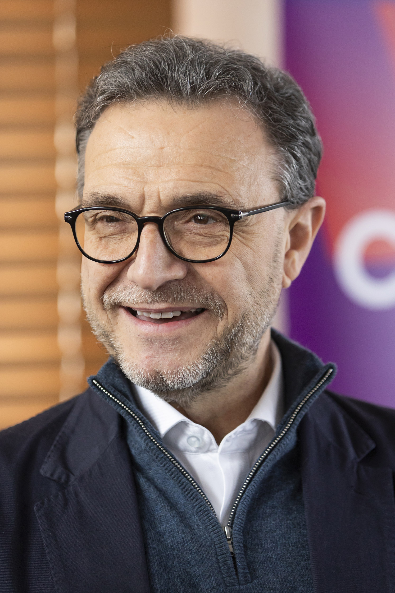 Portrait en couleurs d'un homme aux cheveux poivre et sel, souriant, barbu et portant des lunettes