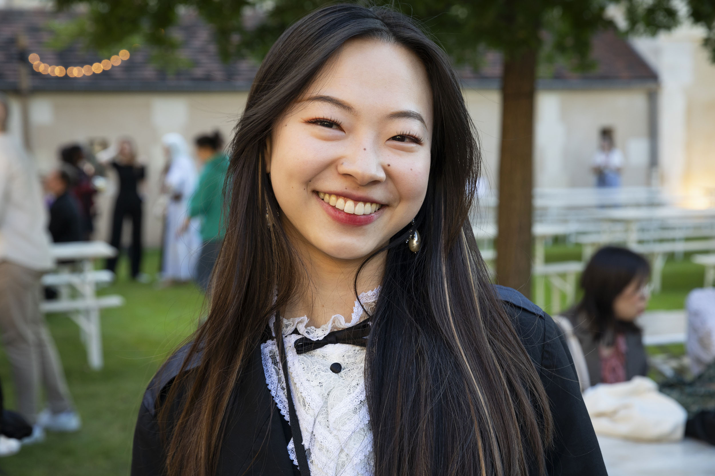 Portrait d'une jeune femme asiatique souriante au cheveux longs, elle est dans un jardin et regarde dans l'objectif