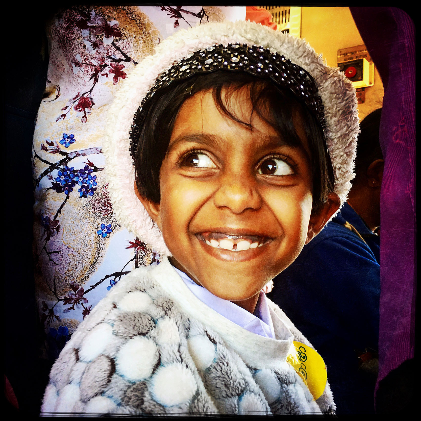 Portrait d'une enfant souriante aux grands yeux portant un bonnet sur la tête dans un train au Sri Lanka