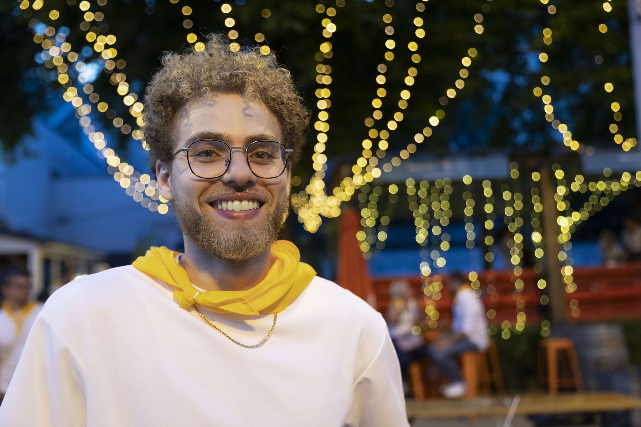 Portrait de nuit d'un jeune homme barbu souriant pendant une soirée festive, des guirlandes lumineuses sont à l'arrière plan