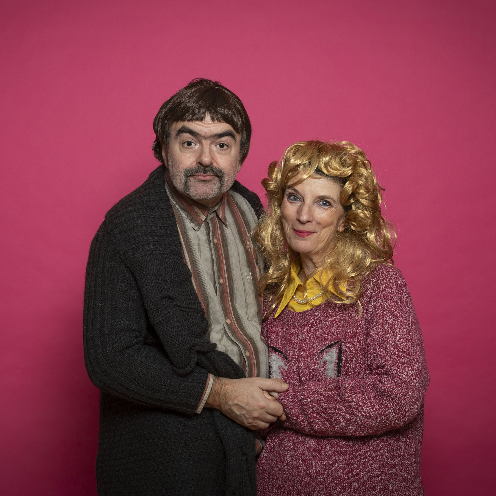 Couple des années 80 en gros pullover sur fond rose qui se tiennent par la main, ils regardent dans l'objectif