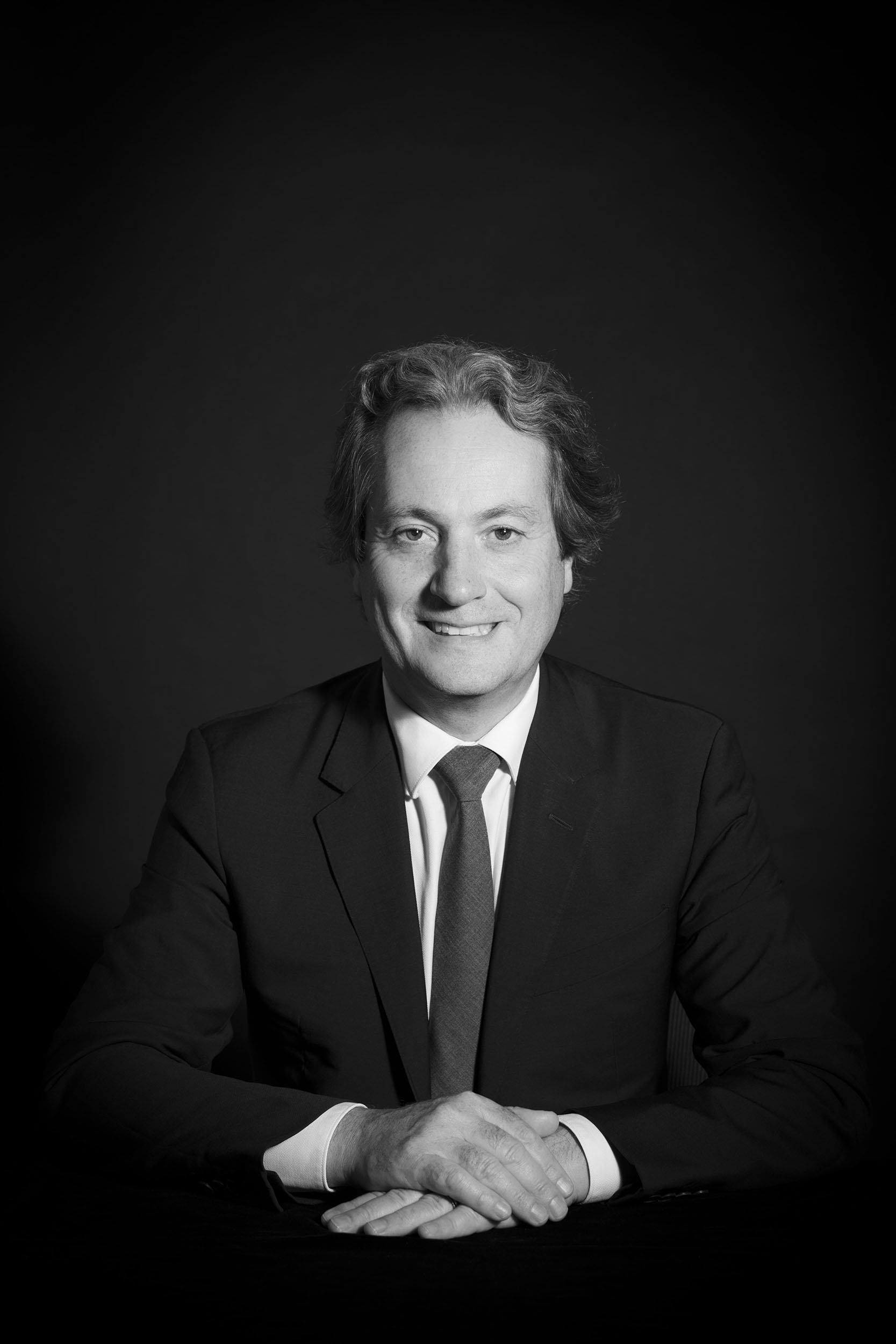 Photographie de portrait corporate en noir et blanc sur fond noir réalisée en studio d'un homme en costume cravate